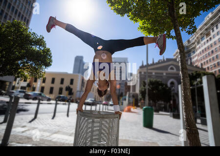 Athletic woman performing handstand and doing split on bin Stock Photo
