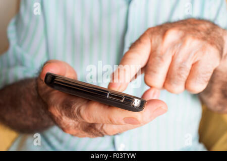 closeup of an old caucasian man sitting in an armchair uses a smartphone Stock Photo