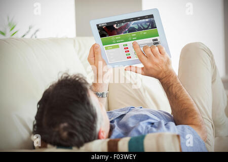 Composite image of man laying on sofa using a tablet pc Stock Photo