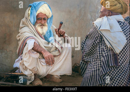 Two aging men dressed traditionally in turbans smoke a clay pipe at the end of the day's camel trading. Stock Photo
