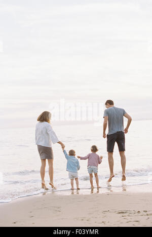 Couple playing with their son and daughter on a sandy beach by the ocean, holding hands.