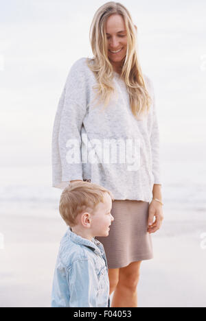 Smiling woman standing on a sandy beach by the ocean with her young son. Stock Photo