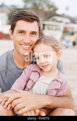 Young girl sitting on her father's lap, looking at camera, smiling. Stock Photo