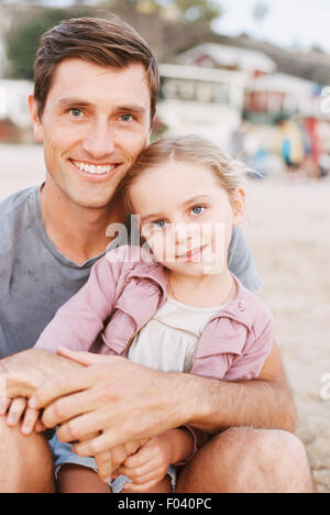 Young girl sitting on her father's lap, looking at camera, smiling. Stock Photo
