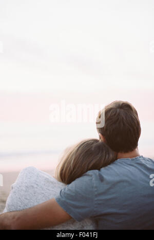 A couple sitting looking out to the ocean, back view, arms around each other. Stock Photo