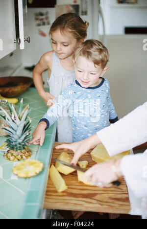 Woman cutting a fresh pineapple for her children. Stock Photo