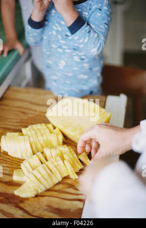 Woman cutting a fresh pineapple for her children. Stock Photo