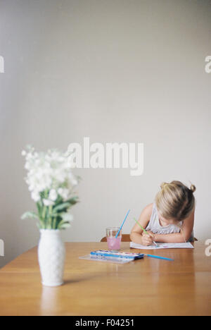 Young girl sitting at  a table, painting, a vase with white flowers. Stock Photo