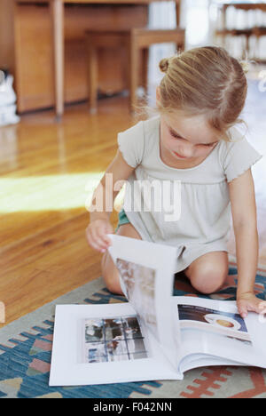Young girl sitting on the floor, reading a lifestyle magazine. Stock Photo