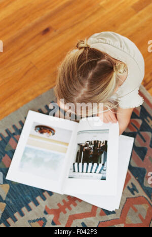 Young girl sitting on the floor, reading a book, view from above Stock Photo