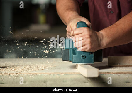 Carpenter working with electric planer on wooden plank in workshop. Stock Photo