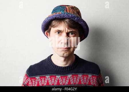 Young handsome man in knit colourful clothes, gray wall behind Stock Photo
