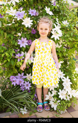 Portrait of a beautiful little girl in summer dress, clematis flowers on background Stock Photo