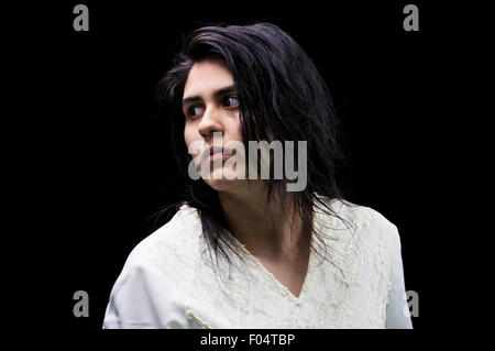 Latina teenager in white standing in front of a black background and looking over her shoulder with a serious expression on her Stock Photo