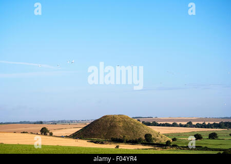 Distant shot of Silbury Hill, man-made Neolithic mound in England. A 40 meter high man-made grass mound standing tall in the relatively flat landscape. Stock Photo