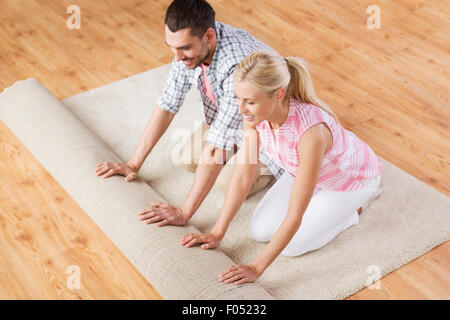 happy couple unrolling carpet or rug at home Stock Photo