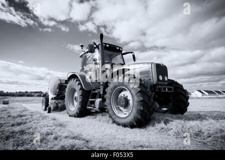 a huge tractor collecting haystack in the field in a nice blue sunny ...