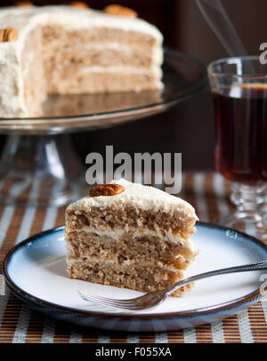 A slice of Hummingbird cake made with banans and pineapple with a cup of coffee and the whole sliced cake in background Stock Photo