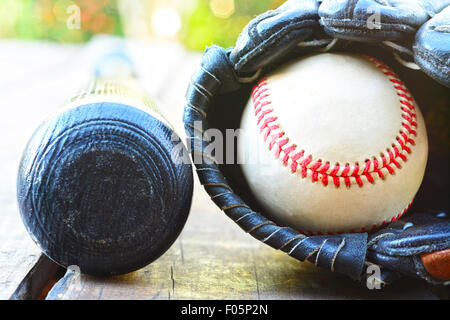 Old bat and ball inside a glove resting on a wooden table Stock Photo