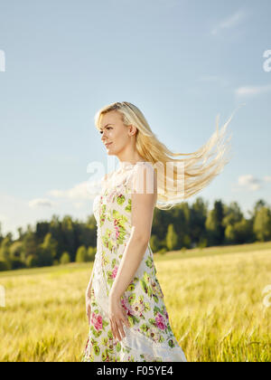 Beautiful fair skin blonde wearing a floral dress, summer sunlight, barley field on background Stock Photo