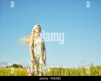 Beautiful fair skin blonde wearing a floral dress, summer sunlight, barley field on background Stock Photo