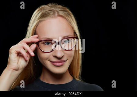 Young attractive blonde woman smiling with hand on her glasses Stock Photo