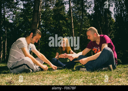 Three friends having fun by playing cards in the forest Stock Photo
