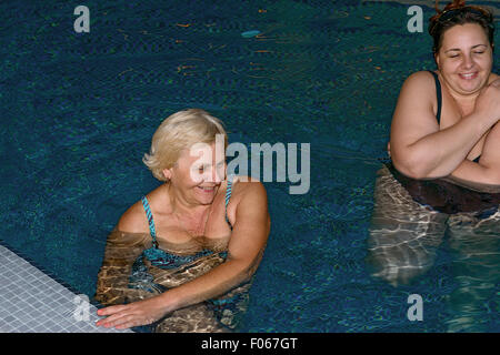 Two women, senior blonde mother and mid adult brunette daughter are doing spa exercises in the water of swimming pool. Stock Photo