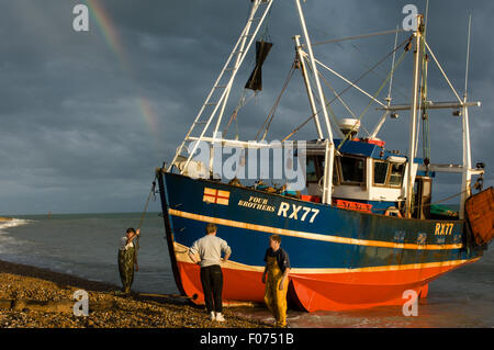 Hastings, East Sussex, England. Hastings, East Sussex, England.  Fishing boat Four Brothers on shoreline with rainbow and three fishermen in the afternoon sun. Stock Photo