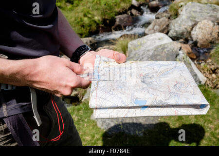 Hiker holding a hiking map and using a navigation compass to measure distance navigating on a hike in Snowdonia National Park. Wales UK Britain Stock Photo