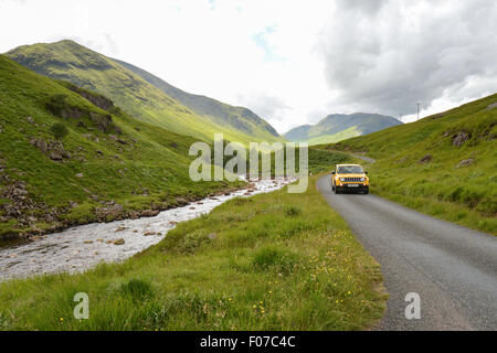 Yellow jeep driving along single track road through Glen Etive, near Glencoe in the Scottish Highlands Stock Photo
