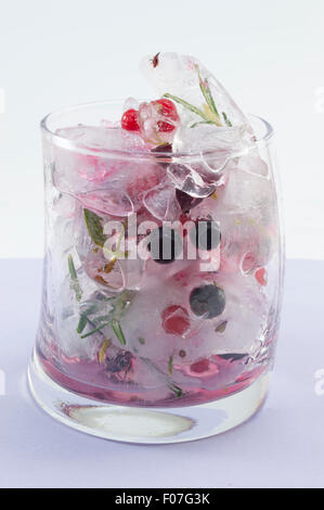 Red forest fruit cocktail with ice, lemon and sliced fruits in a crooked glass on purple background Stock Photo