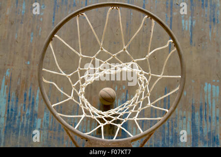 Basketball on wooden floor through a net on metal rim. Stock Photo