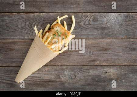Fish and chips. Overhead view fried fish fillet with french fries wrapped by paper cone, on wooden background. Stock Photo