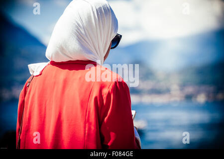 Muslim woman while using smartphone, in the background the lake of garda blurred, Italy Stock Photo