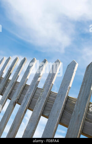 Low angle view, of an old wooden picket fence, against a blue sky with clouds. Stock Photo