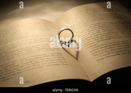 A silver ring casts a heart shaped shadow on an opened book Stock Photo