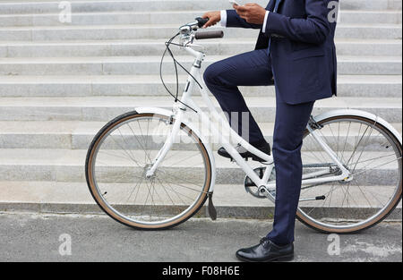 Businessman in suit sitting on bicycle and using cellular phone Stock Photo