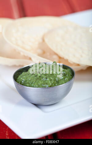 A pile of poppadoms with a bowl of corriander chutney Stock Photo
