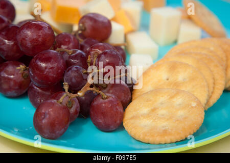 Fresh red grapes sit beside cubes of various cheeses and crackers on a blue and green plate Stock Photo