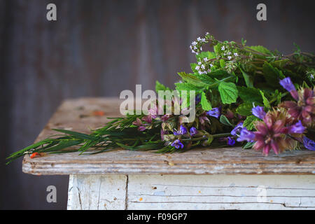 Assortment of fresh herbs mint, oregano, thym, blooming sage over old wooden background. Natural day light. Stock Photo