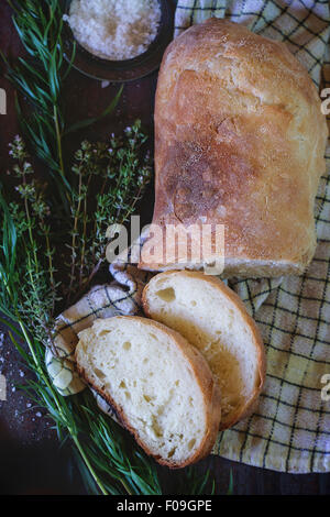 Sliced fresh baked ciabatta bread with salt and herbs thym and oregano. On white checked kitchen towel over metal background. Na Stock Photo