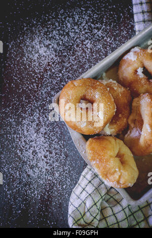 Homemade donuts with sugar and sugar powder in aluminum tray on checkered kitchen towel. Old metal background. Natural day light Stock Photo