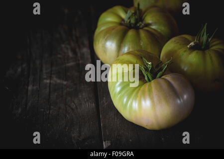 Green unripe big RAF tomatoes over old wooden table. Dark rustic style. Natural day light. With copy space on left Stock Photo