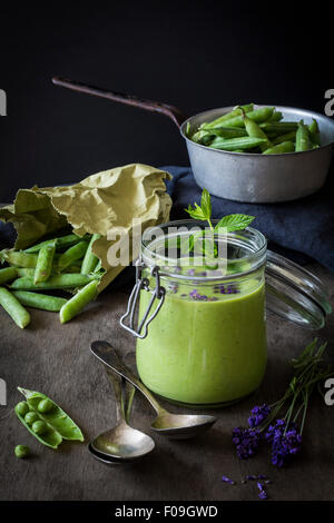 Green gazpacho in jar with peas and lavender on wooden table with vintage colander and spoons Stock Photo