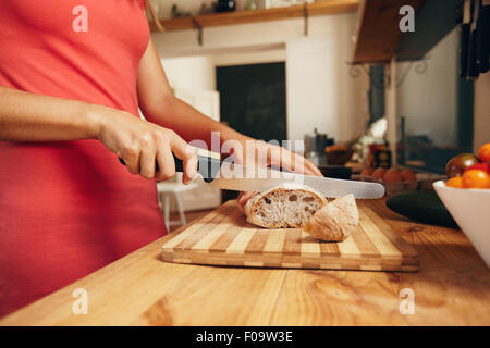 Woman slicing loaf of bread on cutting board with kitchen knife. Close-up shot of female hands cutting bread on kitchen counter, Stock Photo