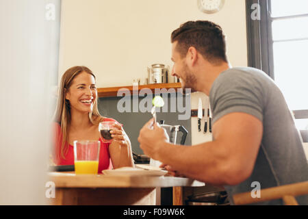 Happy young couple having breakfast at home. Young woman drinking coffee and man eating while sitting at breakfast table togethe Stock Photo