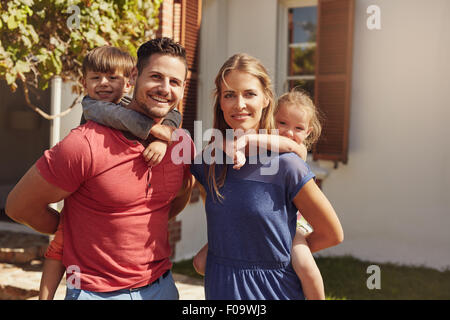 Outdoor shot of a happy couple carrying their children on their backs. Portrait of a mother and father giving their children pig Stock Photo