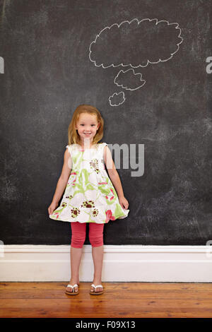 Full length shot of cute young girl in front of chalkboard with a thinking bubble, She is holding her dress looking at camera sm Stock Photo