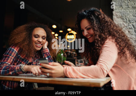 Two young women having fun together and using a smart phone. Happy young female friends sitting together at cafe.